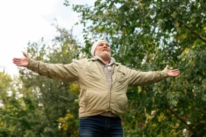 A senior man spreading his arms in joy and embracing the outdoors, symbolizing the relief provided by Oxeze asthma medication.