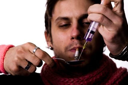 Young addict with heroin syringe injection and spoon