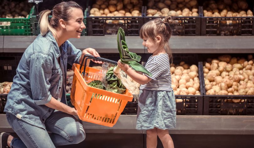 pregnant mother choosing pesticide free organic vegetables with young daughter at grocery store