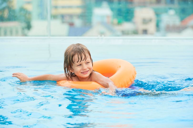 Young girl happily swimming in a pool with clear blue water. Stay mindful of swimming pool bacteria for a safe experience.