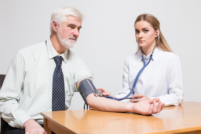 female physician checking high blood pressure signs of a man in his 60's
