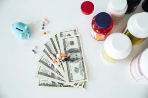 An image depicting pills on top of US dollar bills, alongside a piggy bank and pill bottles, illustrating the implications of the Protecting American Intellectual Property Act