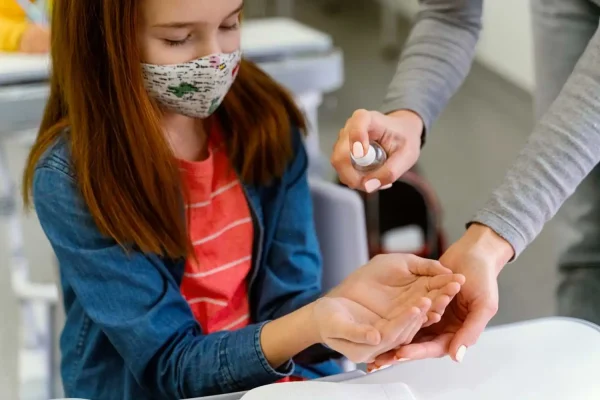 Small girl wearing a face mask extends her hand for sanitizer