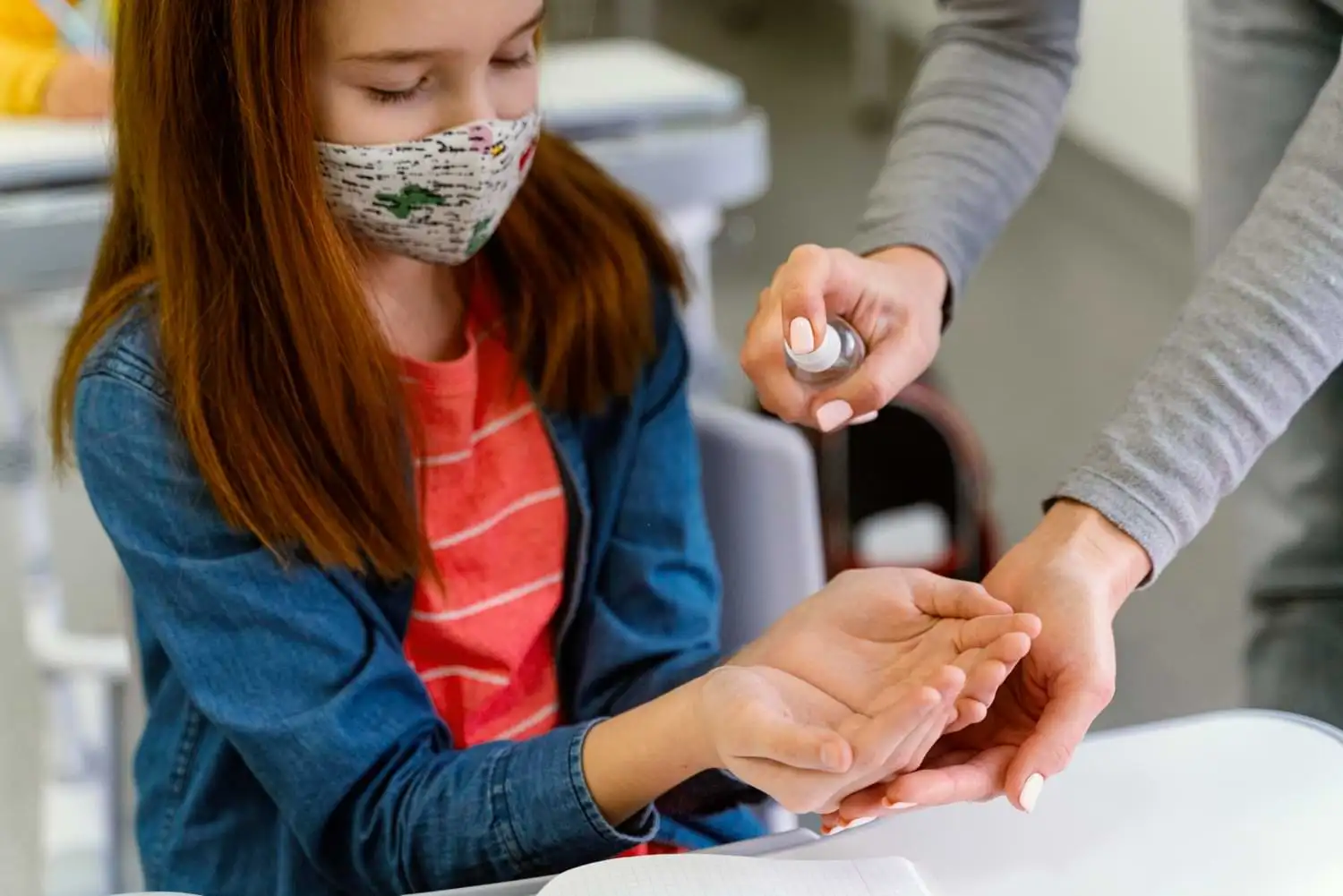 Small girl wearing a face mask extends her hand for sanitizer