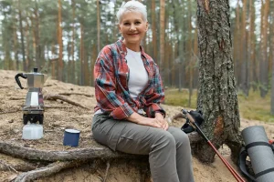 senior woman sitting in a forest with camping gear
