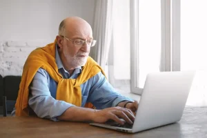 Older man researching if it is safe to buy Eliquis from Canada on his laptop at home