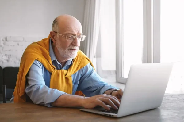 Older man researching if it is safe to buy Eliquis from Canada on his laptop at home
