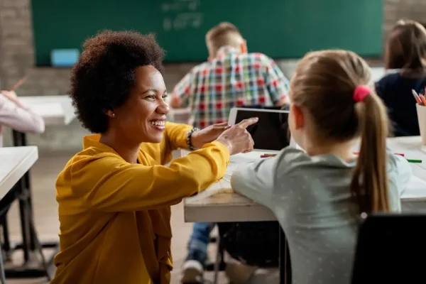 Teacher helping a student in class while discussing ways families can manage medication expenses such as Linzess cost and treatment affordability.