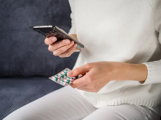 Person checking medication and phone while researching where to buy Clomid online