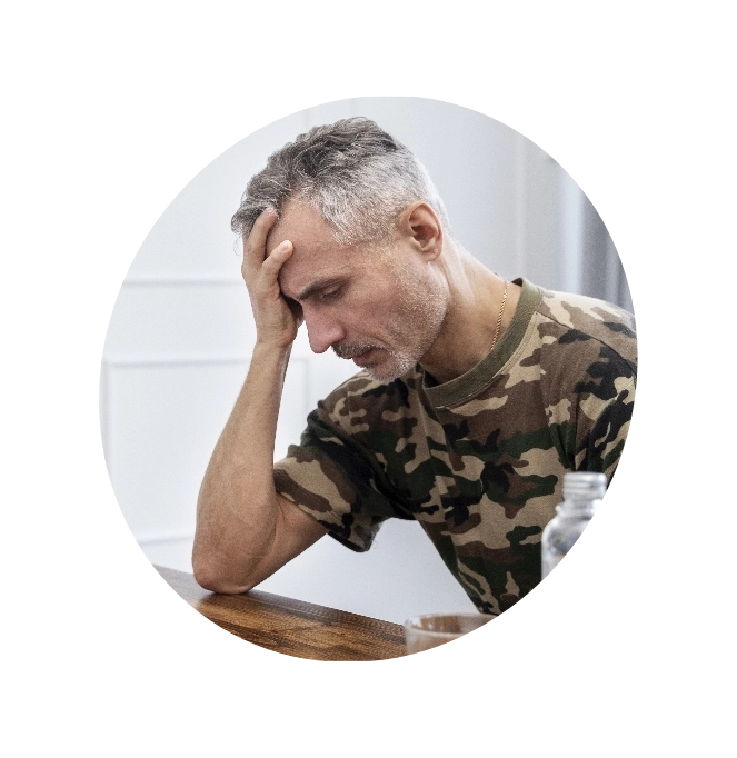 A man in an army T-shirt holding his head and looking down in depression.