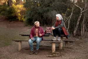 Two active senior women enjoying a conversation outdoors on a park bench during a walk while comparing Eliquis vs Xarelto blood thinner options.