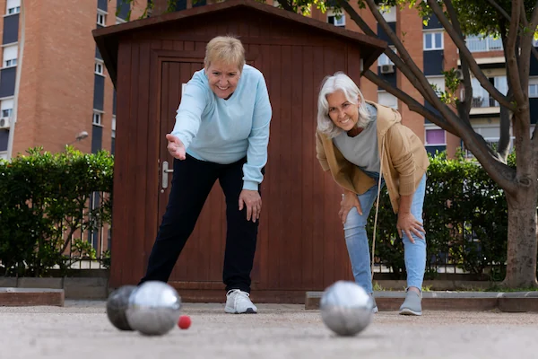 Older adults discussing medication costs while playing bocce, illustrating why Eliquis is so expensive