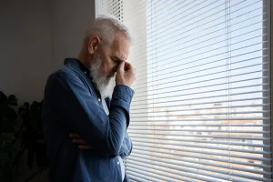 A stressed man sitting in a waiting room holding his head, illustrating why Trintellix is so expensive for patients managing depression.